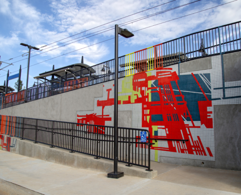 400 feet of mandarin, teal, kiwi & gray tile mosaics in varying sizes with bold, linear architectural patterns on the walking ramps of both sides of Charlotte’s 25th St Station light rail platform. Handrails above each mosaic are powder coated in corresponding colors.