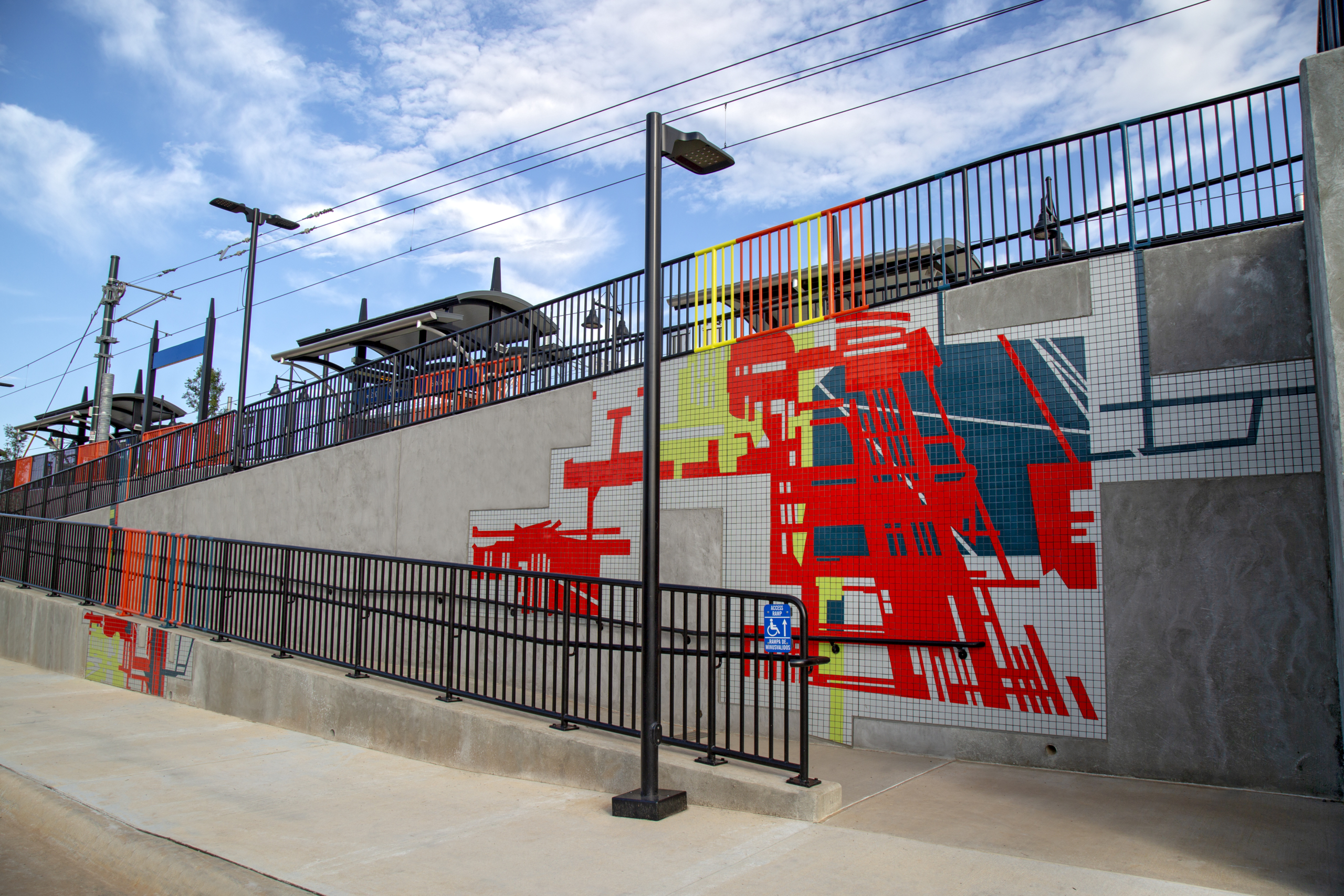 400 feet of mandarin, teal, kiwi & gray tile mosaics in varying sizes with bold, linear architectural patterns on the walking ramps of both sides of Charlotte’s 25th St Station light rail platform. Handrails above each mosaic are powder coated in corresponding colors.