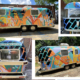 Aluminum Airstream Argosy completely painted in enamel, with images of tools on a brightly-colored background of geometric shapes. Large She Built This City logo in black on side. United We Spark in teal block letters over rear windshield.