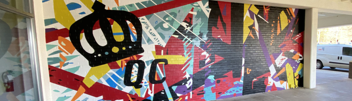 Energetic mural of geometric shapes & abstracted trusses & beams in bold colors on brick wall. Charlotte NC’s crown logo and “QC” painted prominently in black on left side of mural. Located outside Bart’s Bottle Shop, Eastway Shopping Center.