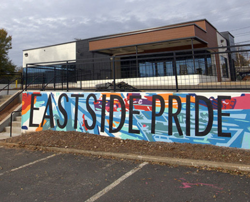 Detail of approx 950 sq ft mural covering multiple walls in Charlotte’s Eastway Crossing mall parking area. Eastside Pride painted in thin, black block letters over a busy, colorful mural of abstract geometric shapes & lines.