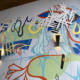 Detail of 16’ h x 50’ w hand-painted mural with vibrantly-colored, energetic, layered leaf-like shapes & shiny aluminum embellishments on stucco breezeway wall of HUB Apartments in Charlotte’s Southend.