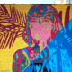 15” h x 24’ w mural on exterior concrete wall of woman painted in vibrant colors with shoulder-length hair facing forward, looking outward. Mural bisected diagonally: yellow background with maroon palm fronds on left side, right side blocked in all blues. In shadows of Ashland Ave L Train bridge, Lakeview Chicago.